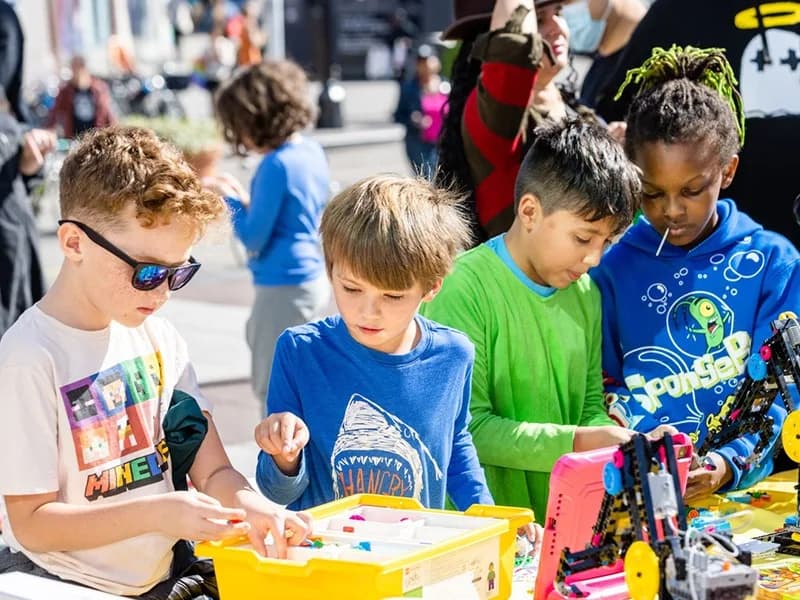 Four children building with LEGO at an outdoor table during a Gensa street event
