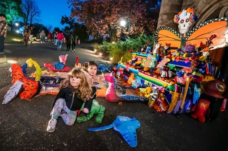 Children sit beside a colorful Day of the Dead altar with papier-mâché decorations at Green-Wood