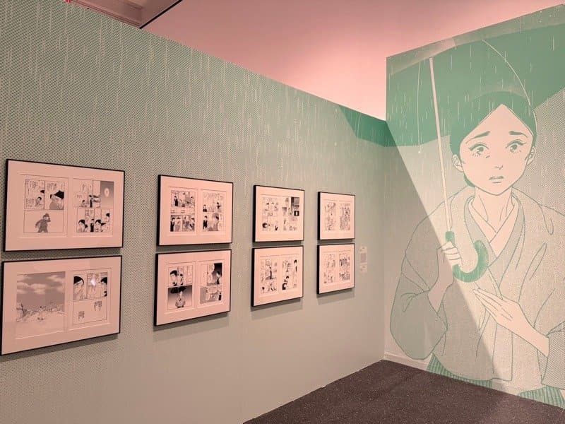 Framed manga pages and a wall mural of a woman holding an umbrella inside The Art of Manga at the Brooklyn Museum
