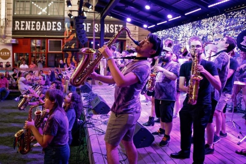 The L Train Brass Band playing saxophones on the outdoor bandshell stage at Industry City at night