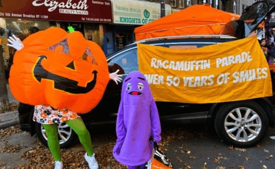 A giant jack-o-lantern costume and a purple monster pose beside a Ragamuffin Parade banner on Third Avenue in Bay Ridge